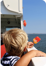 A blond toddler eats a popsicle and watches the waves pass from the deck of a ferry.
