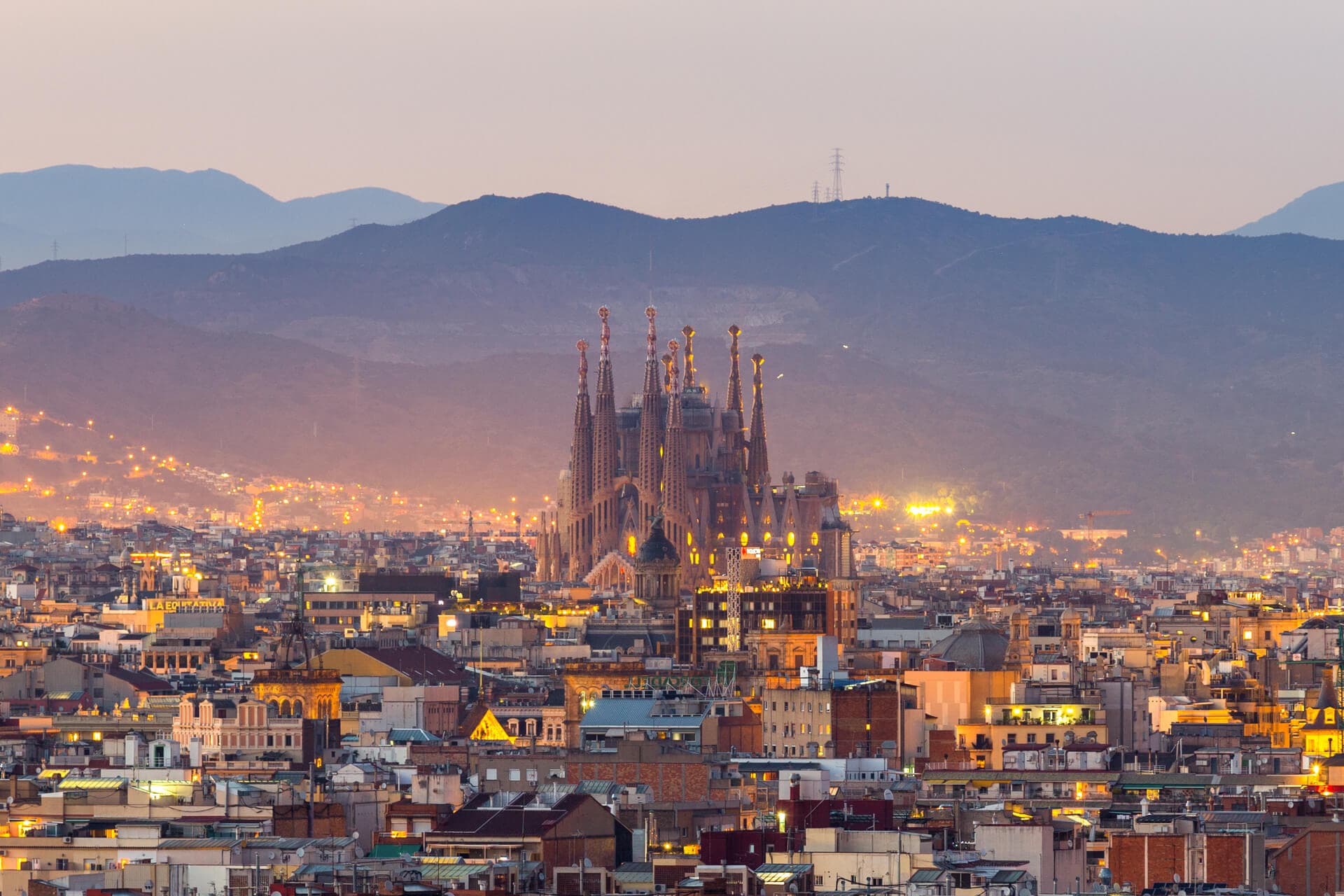 Une photo au coucher du soleil de la ville de Barcelone, avec la Sagrada Familia devant la montagne en toile de fond.