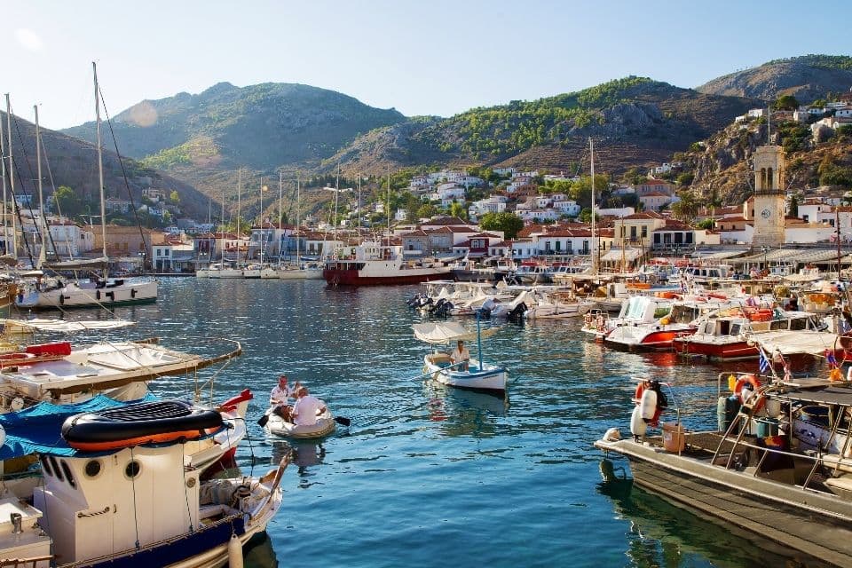 A photo taken during the day by the sea on the island of Hydra. Boats are visible on the sea and mountainous terrain is visible further on.