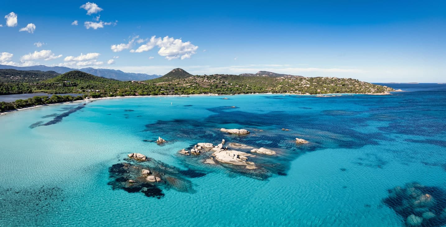Panoramablick auf die türkisfarbene Bucht von Santa Giulia auf Korsika mit Felsen und grünen Hügeln.