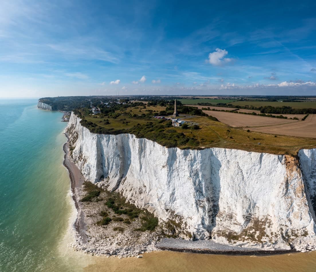Vue aérienne des falaises blanches de Douvres, entourées par une mer bleue et des champs verts.