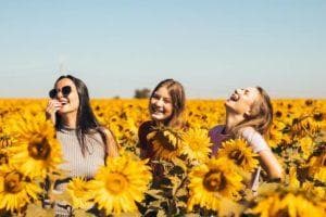 three women standing in a sunflower field together smiling