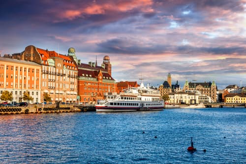 The waterfront of Malmo, Sweden, at dusk, with historic and modern buildings against a sky painted with pink and blue hues.