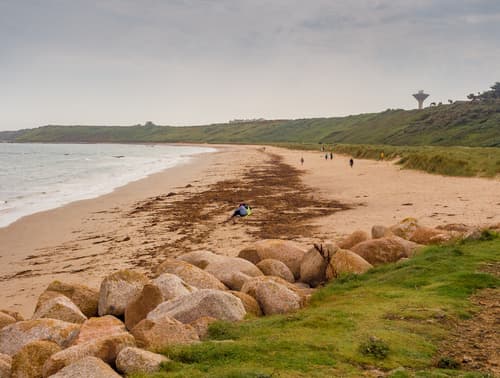 A sandy beach in Rosslare, Ireland, with sparse visitors and a distinctive tower in the distance, under an overcast sky.