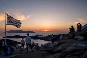 gente visitando la isla de ios de pie sobre las rocas mirando el mar por la noche