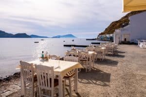mesas y sillas blancas para cenar junto al mar en milos