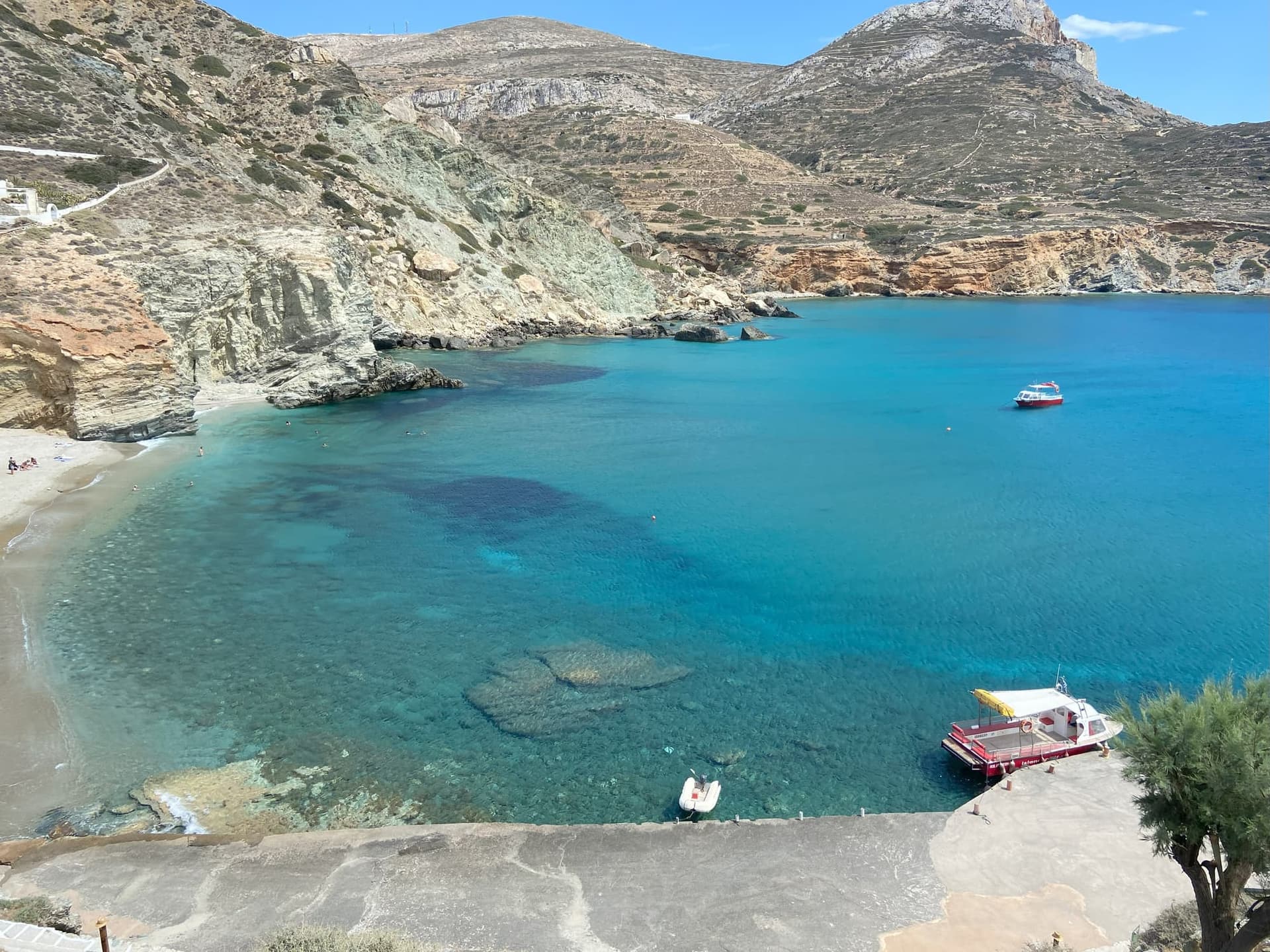 La petite crique d'Agali, entre azur et argenté avec deux petits bateaux sur la surface.