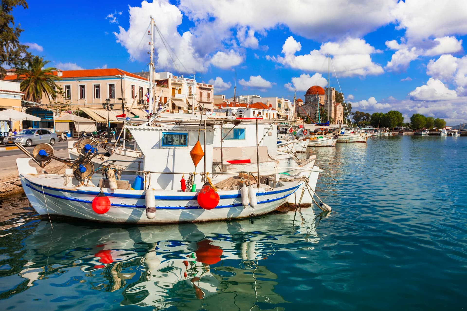 The picturesque port of Aegina, with its colorful caïques, calm waters, and neoclassical buildings along the seafront.