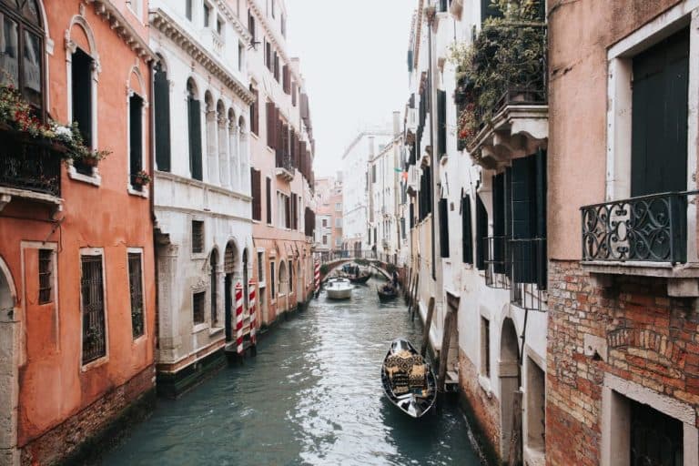 Ein malerischer Kanal in Venedig, Italien, mit traditionellen Gondeln, historischen Gebäuden und einer kleinen Brücke im Hintergrund.
