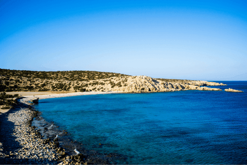 Plage de sable aux eaux bleues entre des collines sablonneuses et sauvages avec une pollution minimale.