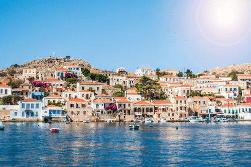 Le pays de Halki avec ses bâtiments blancs aux toits orangés à côté de son port où flottent quelques bateaux.