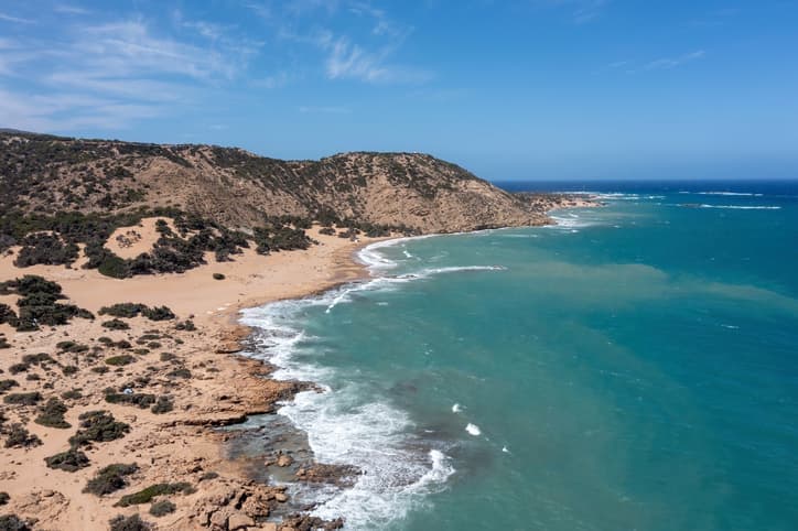 Spiaggia selvaggia di Gavdos con sabbia dorata, scogli e mare turchese sotto un cielo limpido.