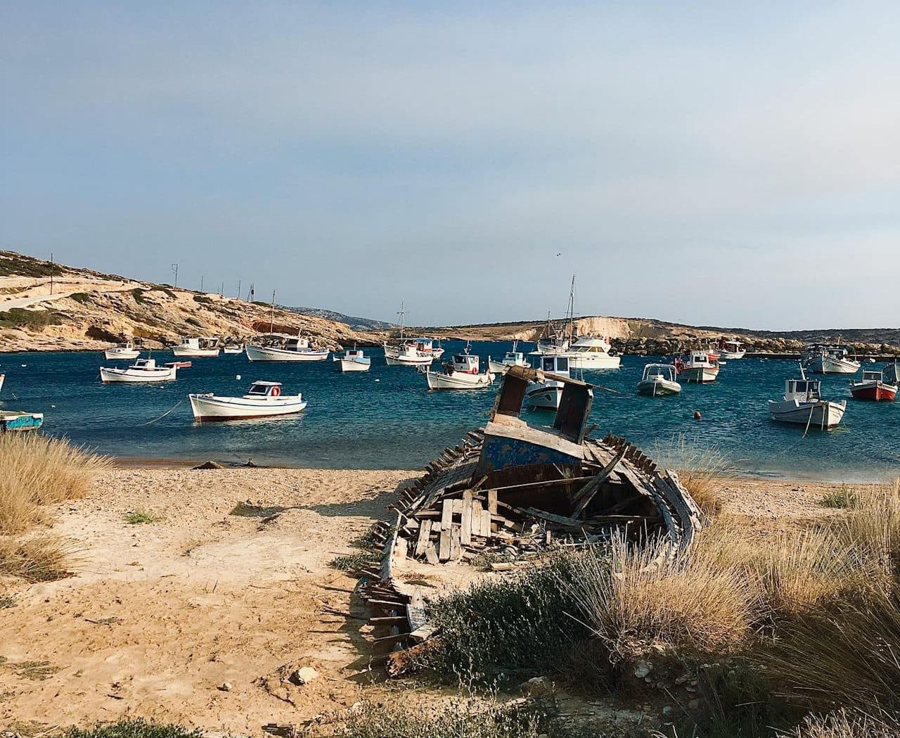 L'épave d'une barque sur une plage devant un petit port de plaisance.