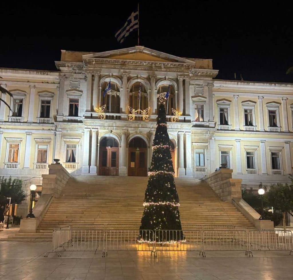H Ερμούπολη της Σύρου, με το στολισμένο δέντρο να φωτίζει την πλατεία και το επιβλητικό Δημαρχείο να ολοκληρώνει το σκηνικό.
