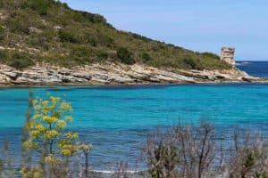 Une berge rocheuse au-dessus d'une crique azure où trône une petite tour de guet de pierre.