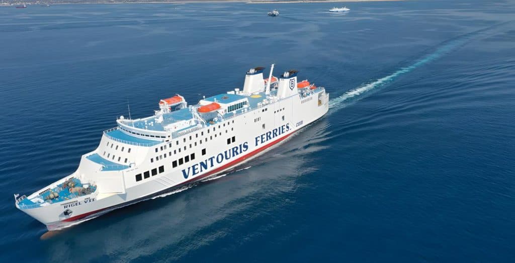 Traghetto Ventouris Ferries in navigazione su un mare calmo, con la scia che si apre dietro la poppa sotto un cielo limpido.