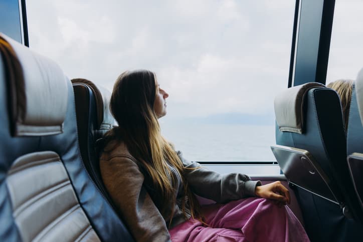 Νεαρή γυναίκα ταξιδεύει με πλοίο, κοιτάζοντας τη θάλασσα από το παράθυρο.