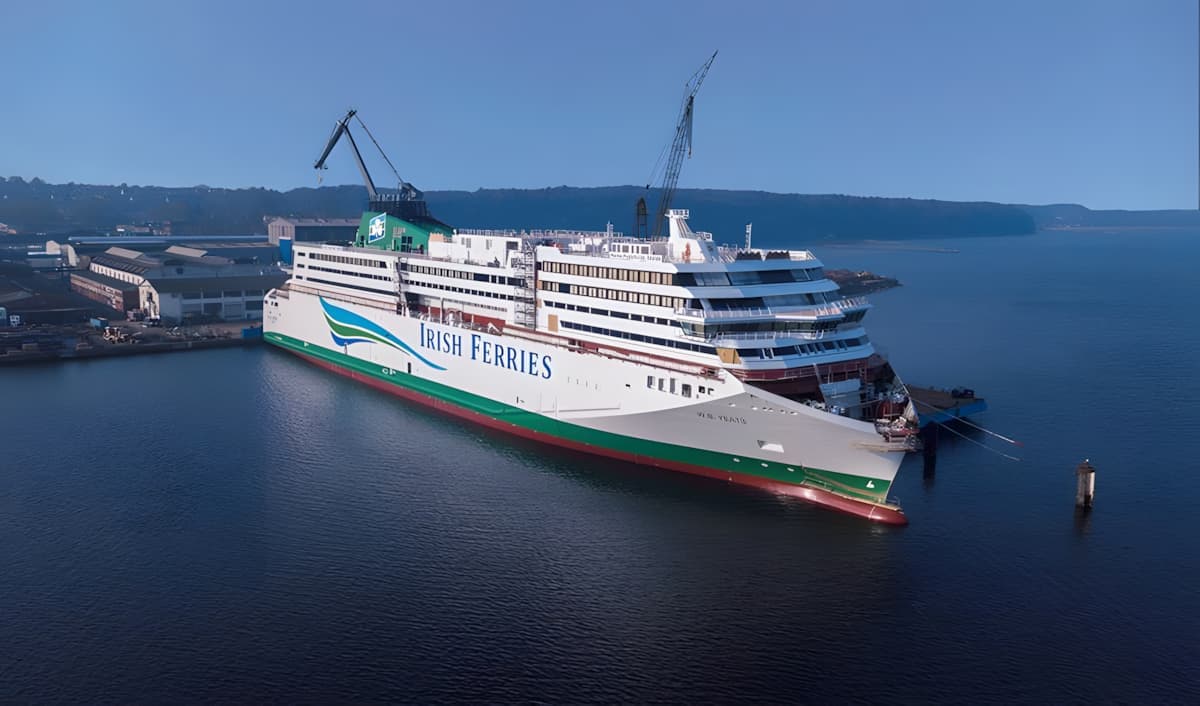 Le ferry WB Yeats d'Irish Ferries amarré dans un chantier naval, avec des grues au-dessus et des eaux calmes reflétant le navire. 