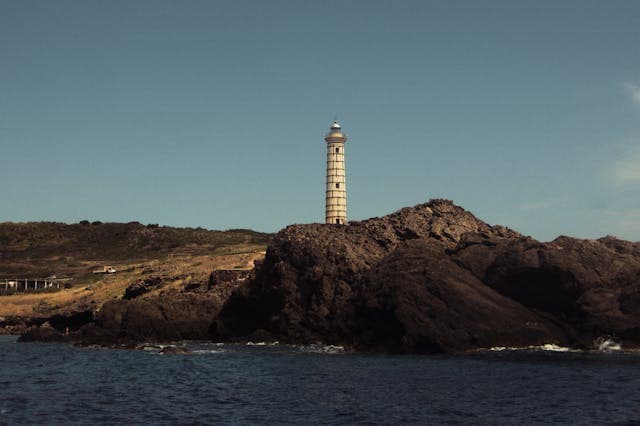 Imponente faro situato su una scogliera rocciosa, con il mare in primo piano sull'isola di Ustica
