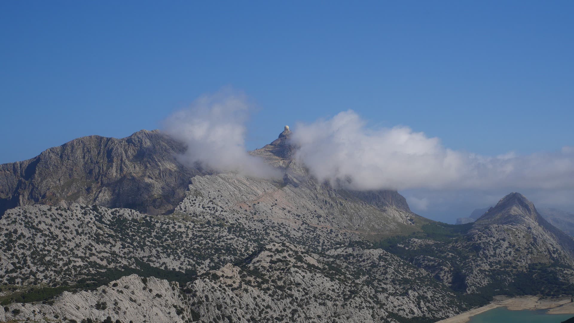 Von Wolken umgebene Berge mit einem darunter liegenden See.