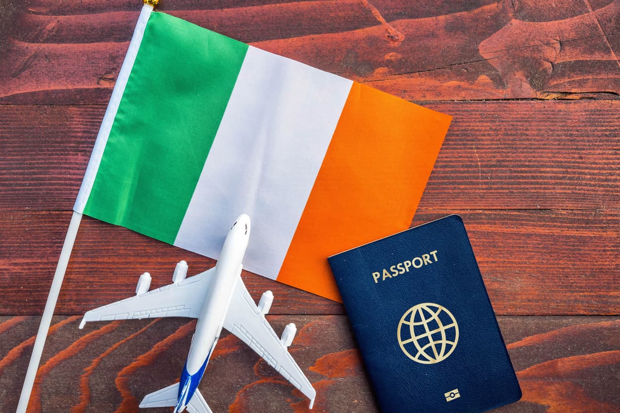 An Irish flag (green, white and orange), a miniature plane and a blue passport.