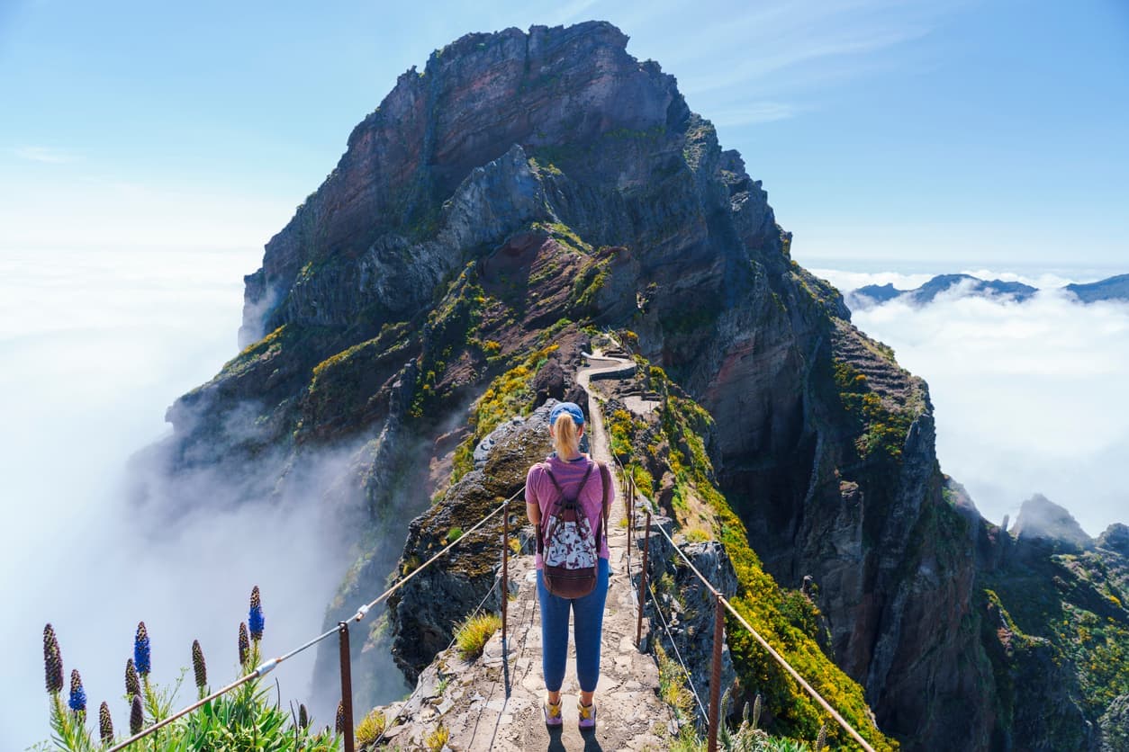 Wanderin auf einem schmalen Bergpfad in Madeira, Portugal, umgeben von steilen Felsen und Wolken.