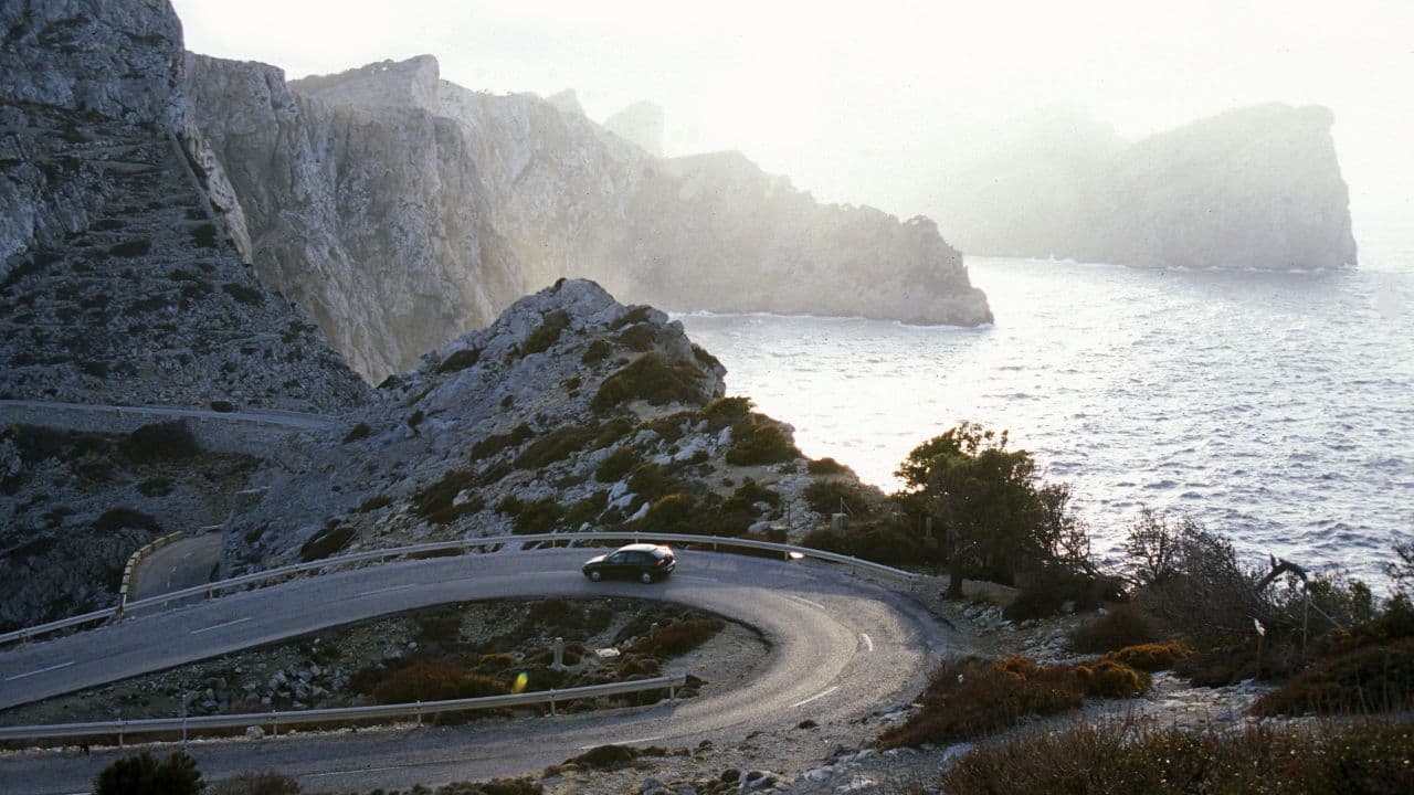 Cap de Formentor auf Mallorca bei Sonnenuntergang mit Auto in der Kurve.