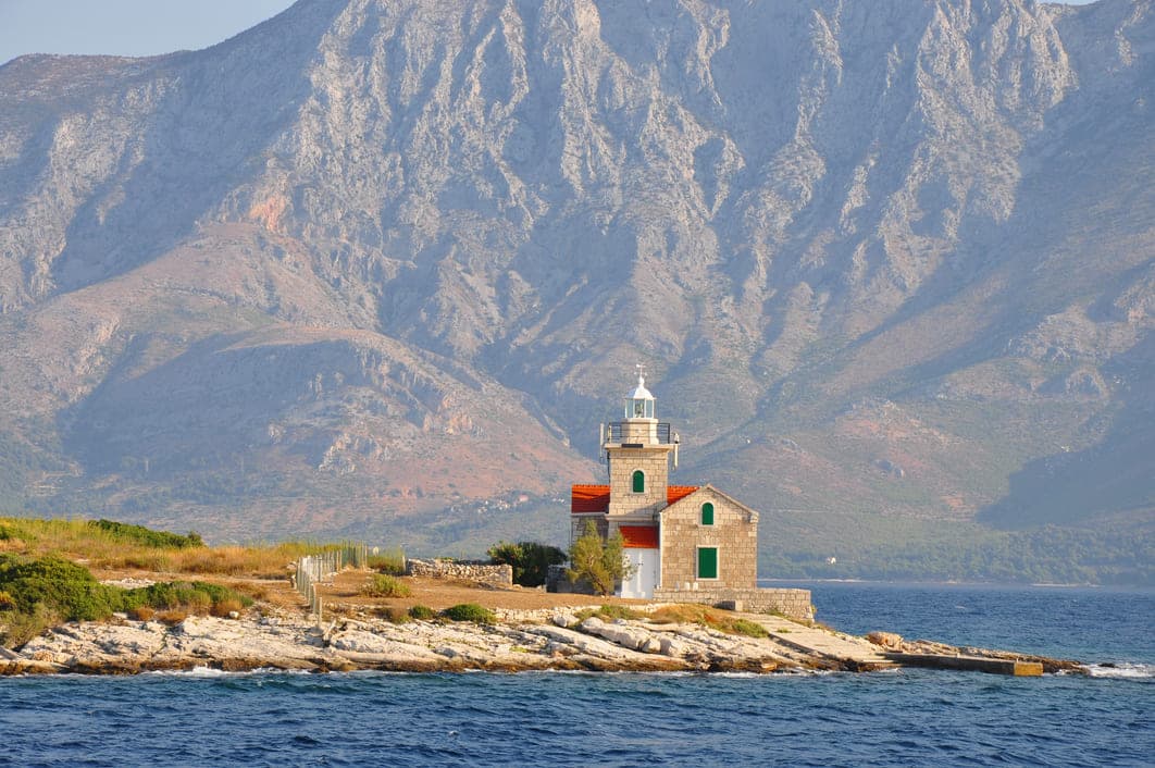 Kameni svjetionik n sa zelenim prozorima i planinom u pozadini