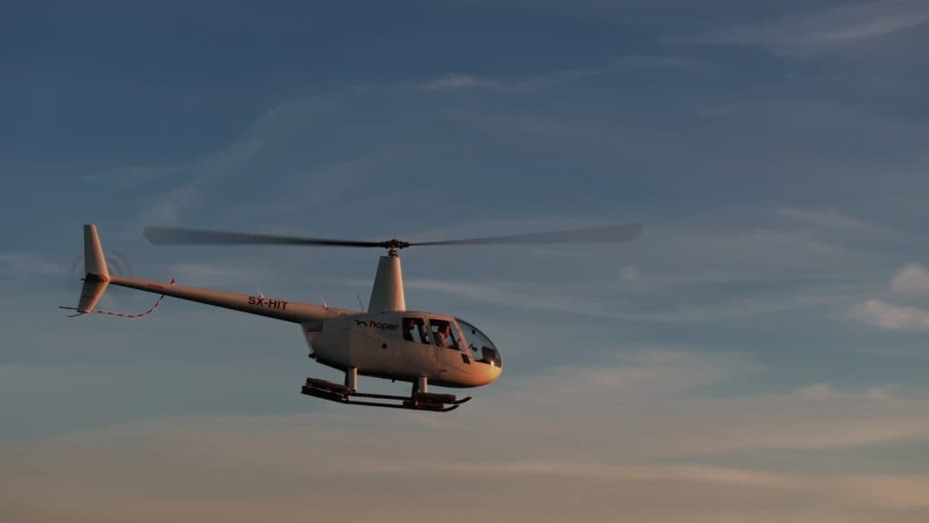 An orange hoper helicopter lands on a Greek Island at sunset.