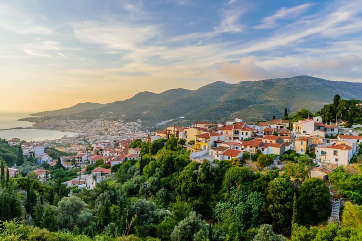 An aerial view of Samos Island at sunset. Green trees and houses line the slopes parallel to the sea.