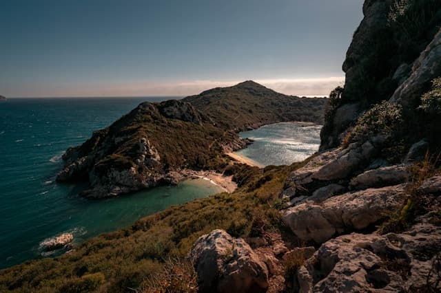 Veduta panoramica della spiaggia di Porto Timoni a Corfù, con due baie di sabbia separate da un istmo e circondate da vegetazione mediterranea.