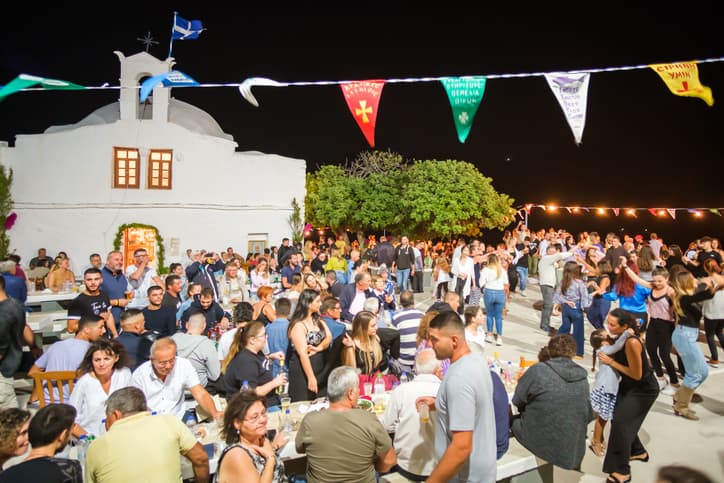 Les rues animées d'Ios après la tombée de la nuit avec une foule et des guirlandes lumineuses.