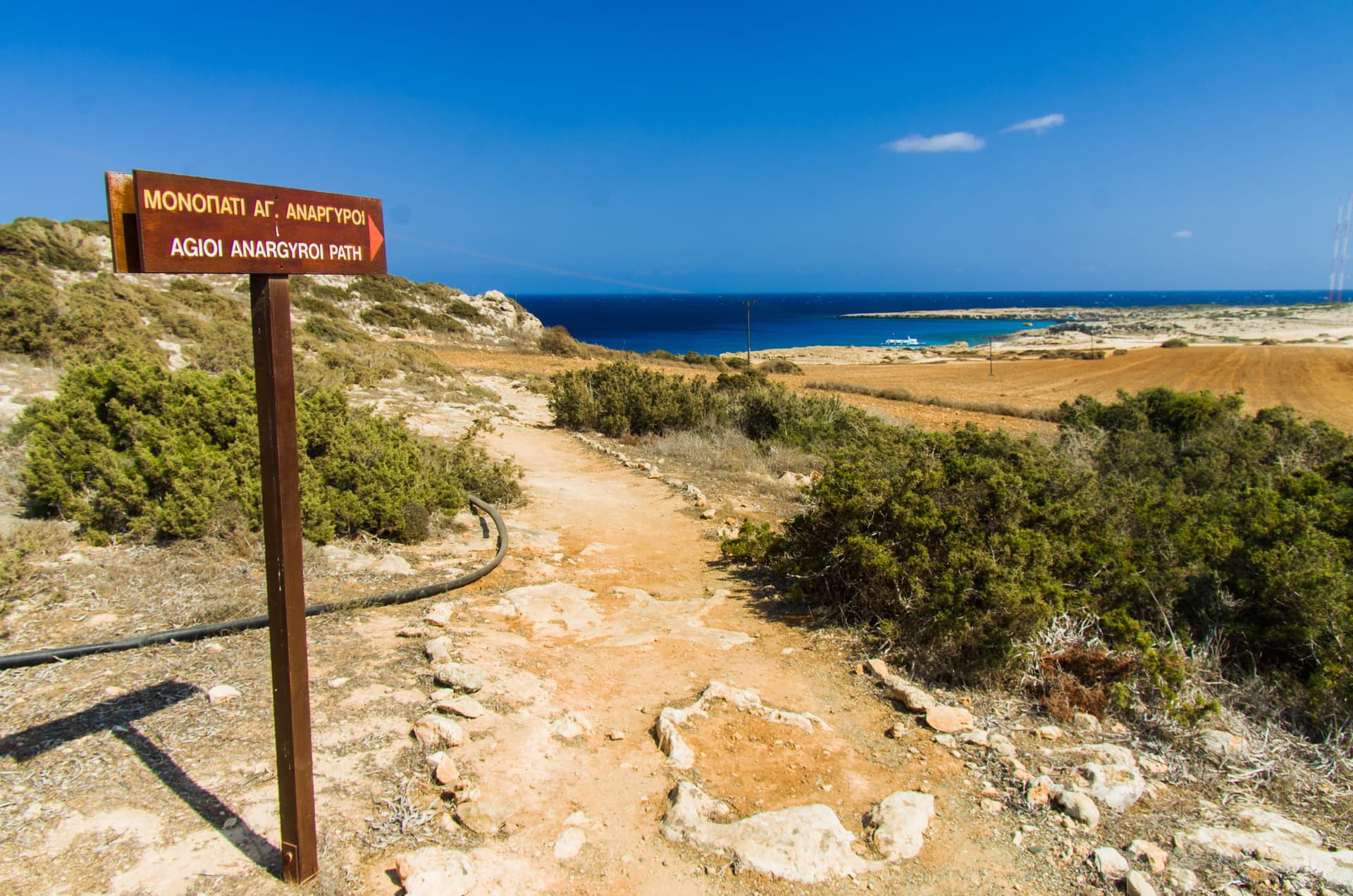 Une pancarte qui indique la plage de Agioi Anargyroi devant un paysage paradisiaque.