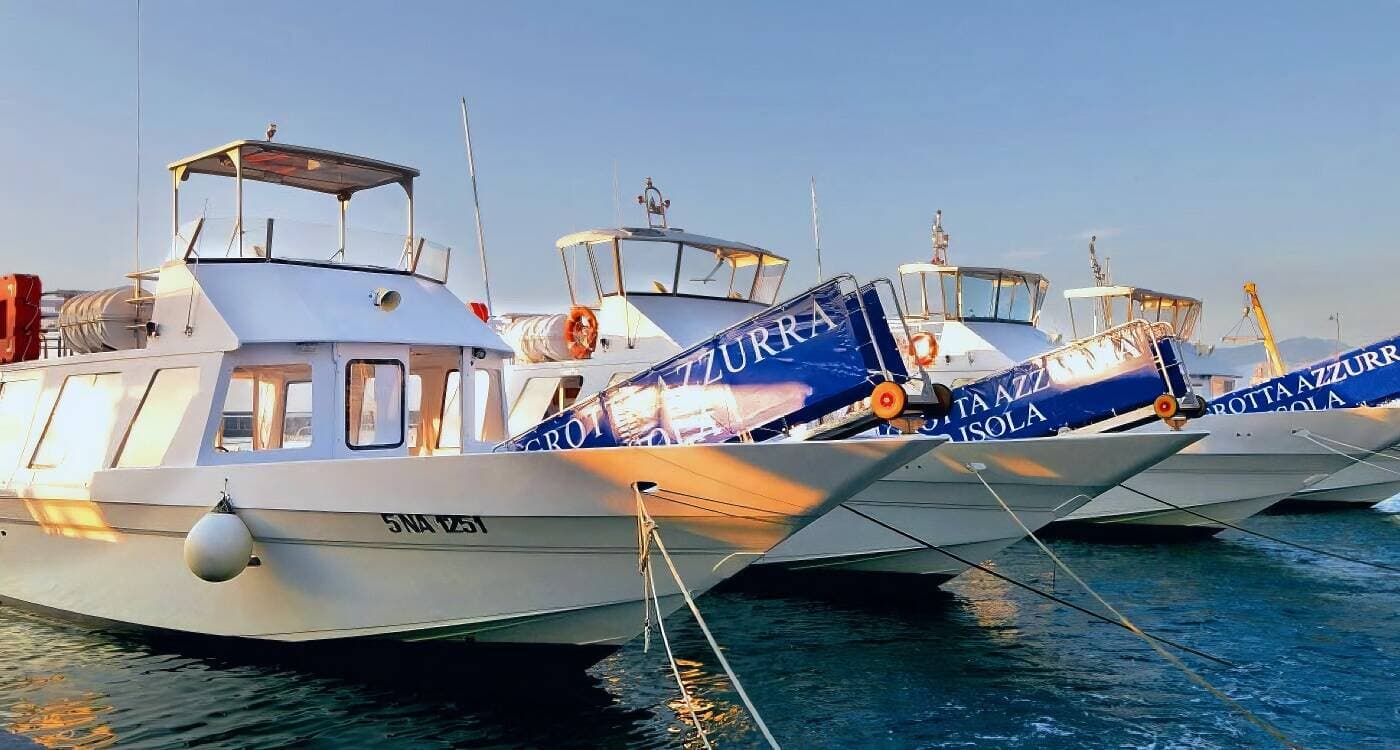 White Laser Capri boats docked side by side at the port, with boarding ramps marked ‘Grotta Azzurra’ reflecting the evening sunlight.