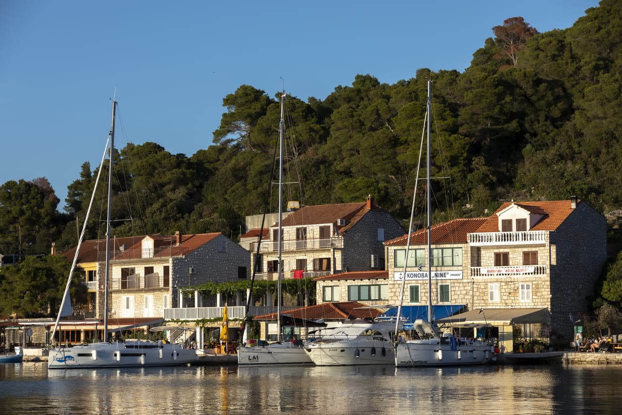 Kamene kućice i brodovi u luci Pomena sa zelenim drvećem u pozadini na otoku Mljetu.