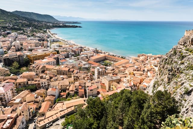 Veduta panoramica di Cefalù in Sicilia, con il centro storico, i tetti color terracotta e la lunga spiaggia bagnata dal Mar Tirreno.