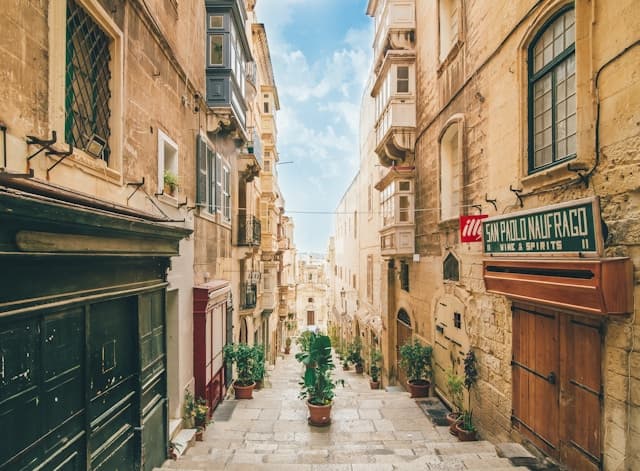 Stradina storica nel centro di La Valletta, Malta, con edifici in pietra, balconi tipici e vasi di piante lungo la scalinata.
