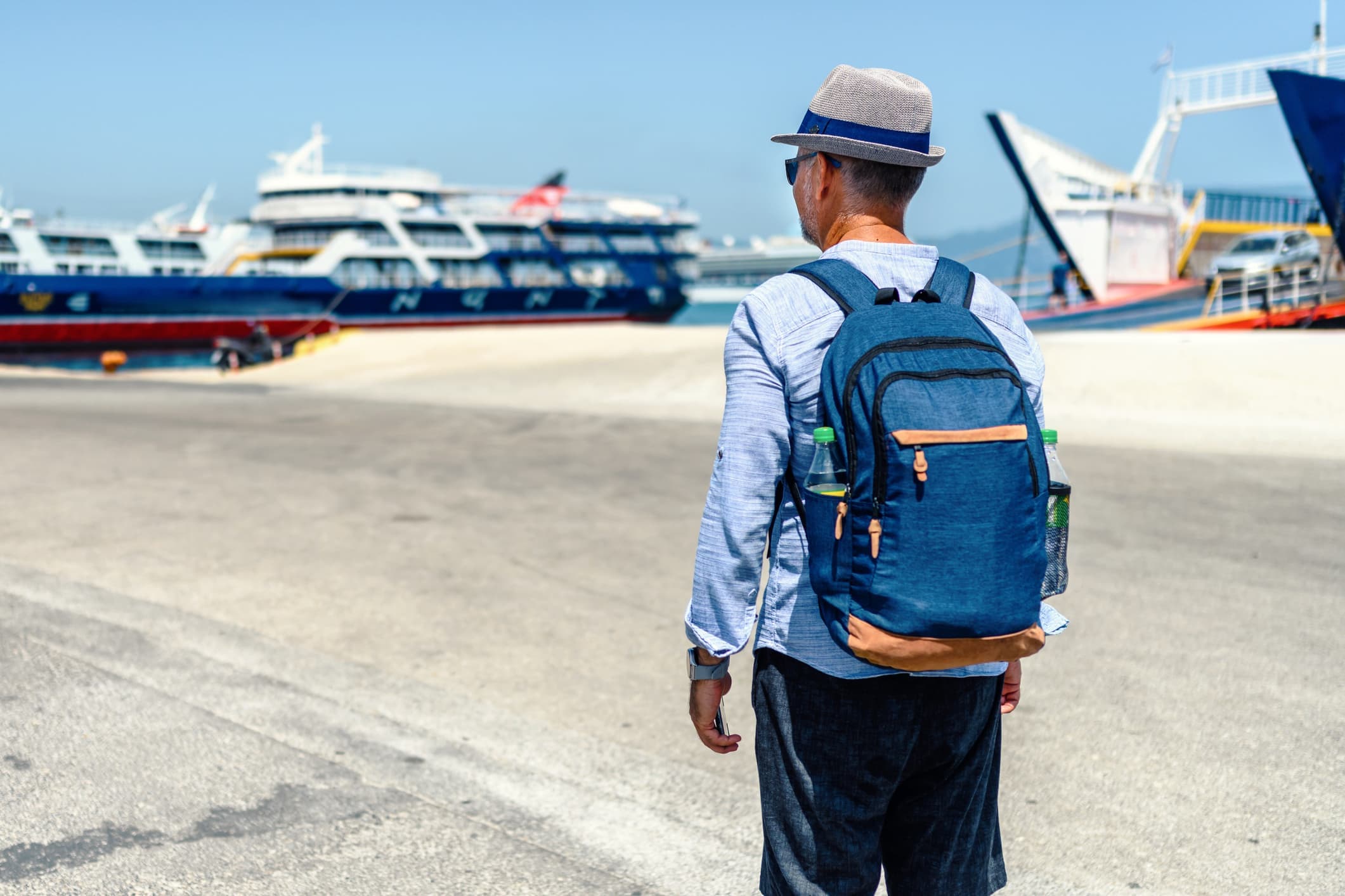 Uomo con zaino e cappello di paglia osserva i traghetti attraccati al porto, pronto per l’imbarco.