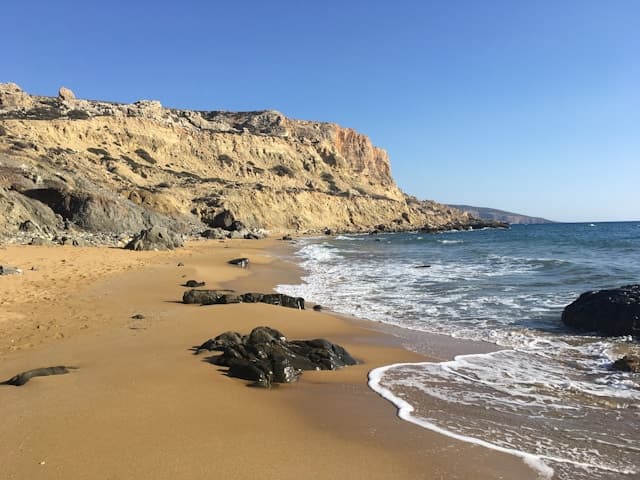 Spiaggia selvaggia con sabbia dorata e scogli neri levigati dal mare sull'isola di Creta.