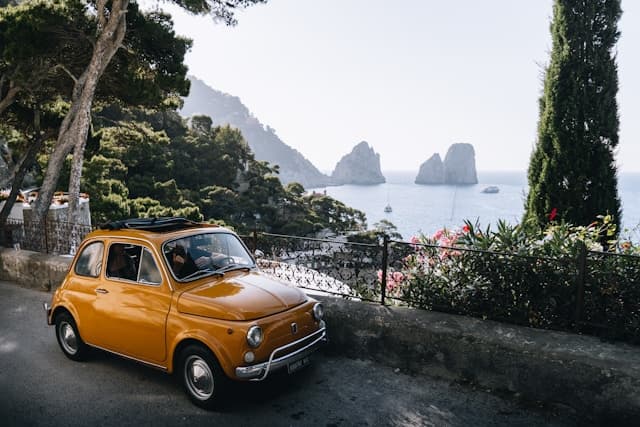 Fiat 500 d’epoca di colore giallo parcheggiata lungo una strada panoramica sull’isola di Capri, in Italia