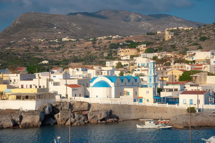 Beyaz evleri, mavi kubbeli kilisesi ve balıkçı tekneleriyle Kasos limanının görünümü.