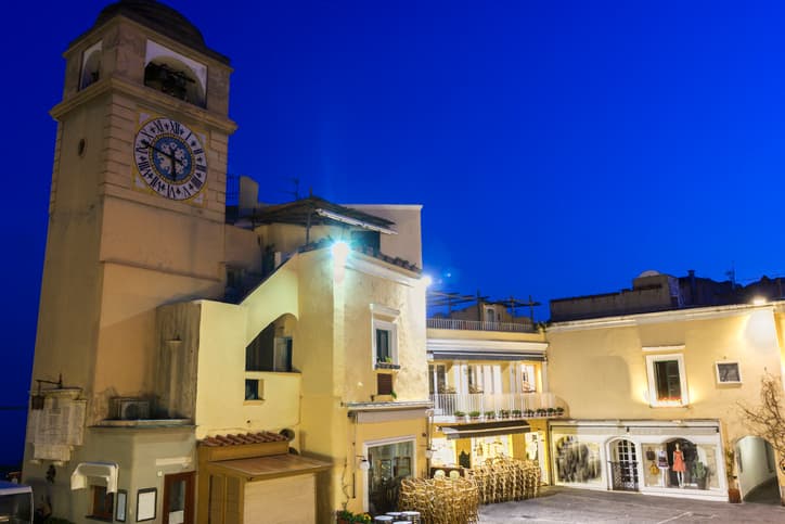 Piazzetta di Capri al tramonto, con il caratteristico campanile con l’orologio illuminato contro il cielo blu della sera.