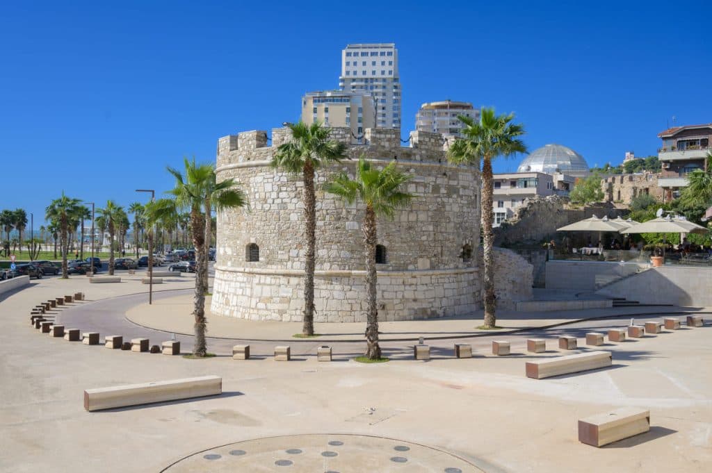 Torre Veneziana di Durazzo sul lungomare, con palme e edifici moderni sullo sfondo.