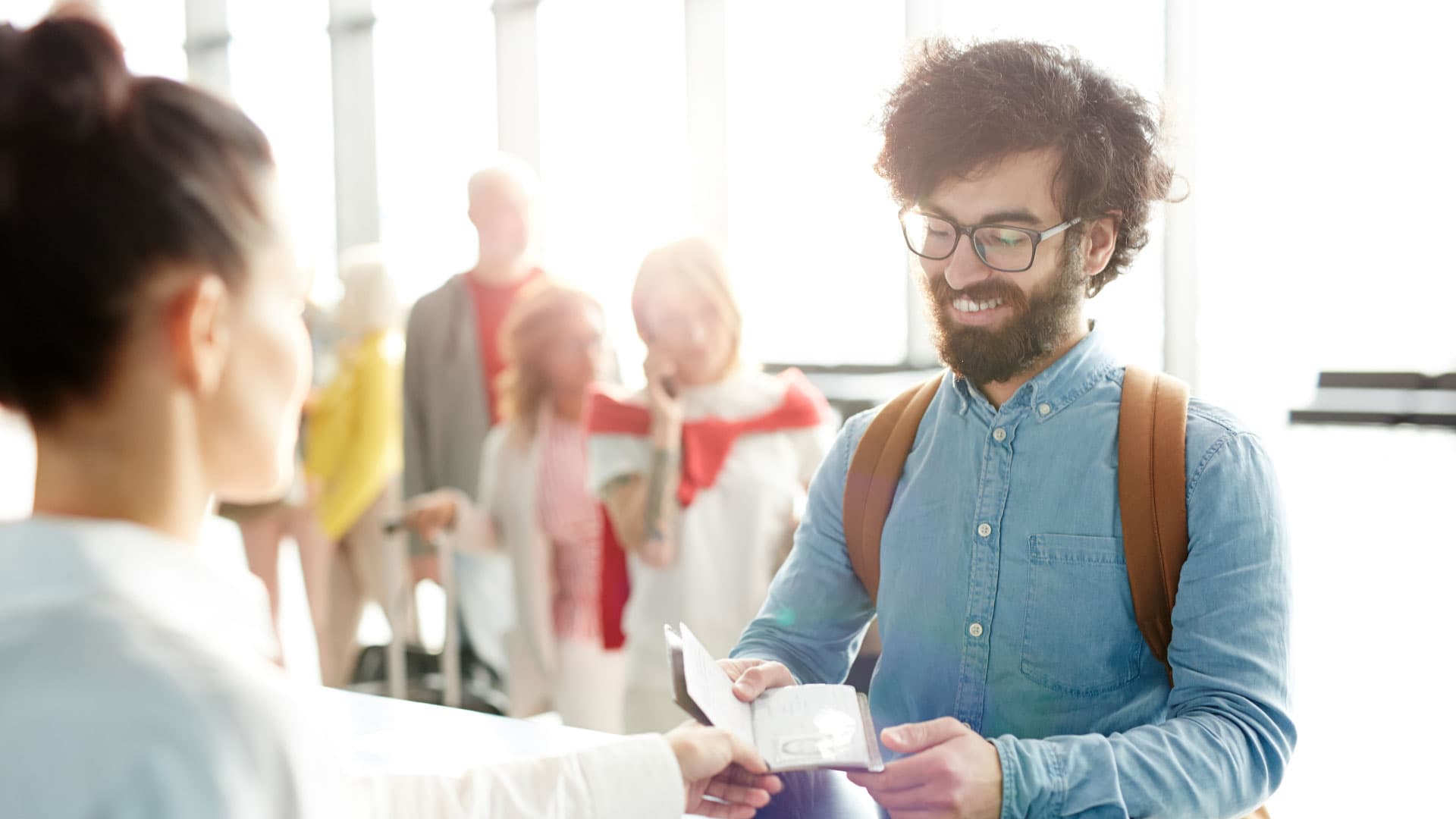 AB vatandaşı olmayan bir kişi güneşli bir havaalanında pasaportunu sınır kontrol görevlisine teslim eder.