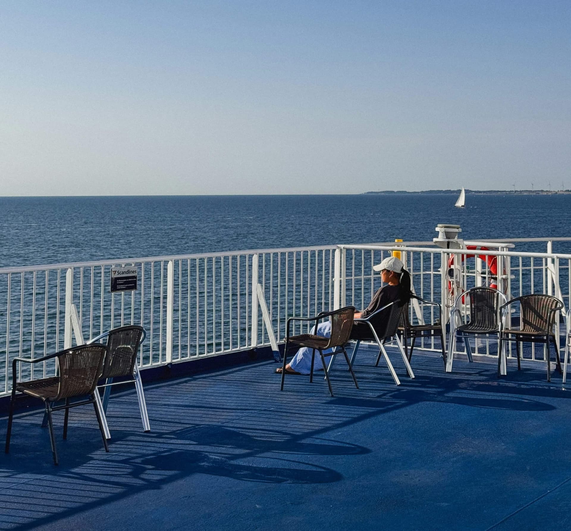 A woman in a sunhat overlooks the horizon of the sea on a ferry's top deck.