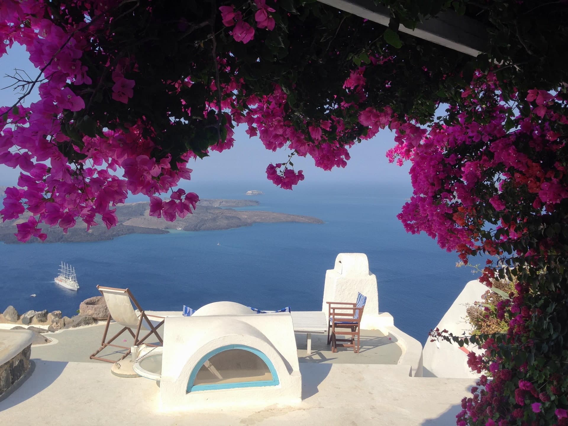 Un arbre à fleurs roses devant une terrasse d'une maison typique de l'île de Santorin