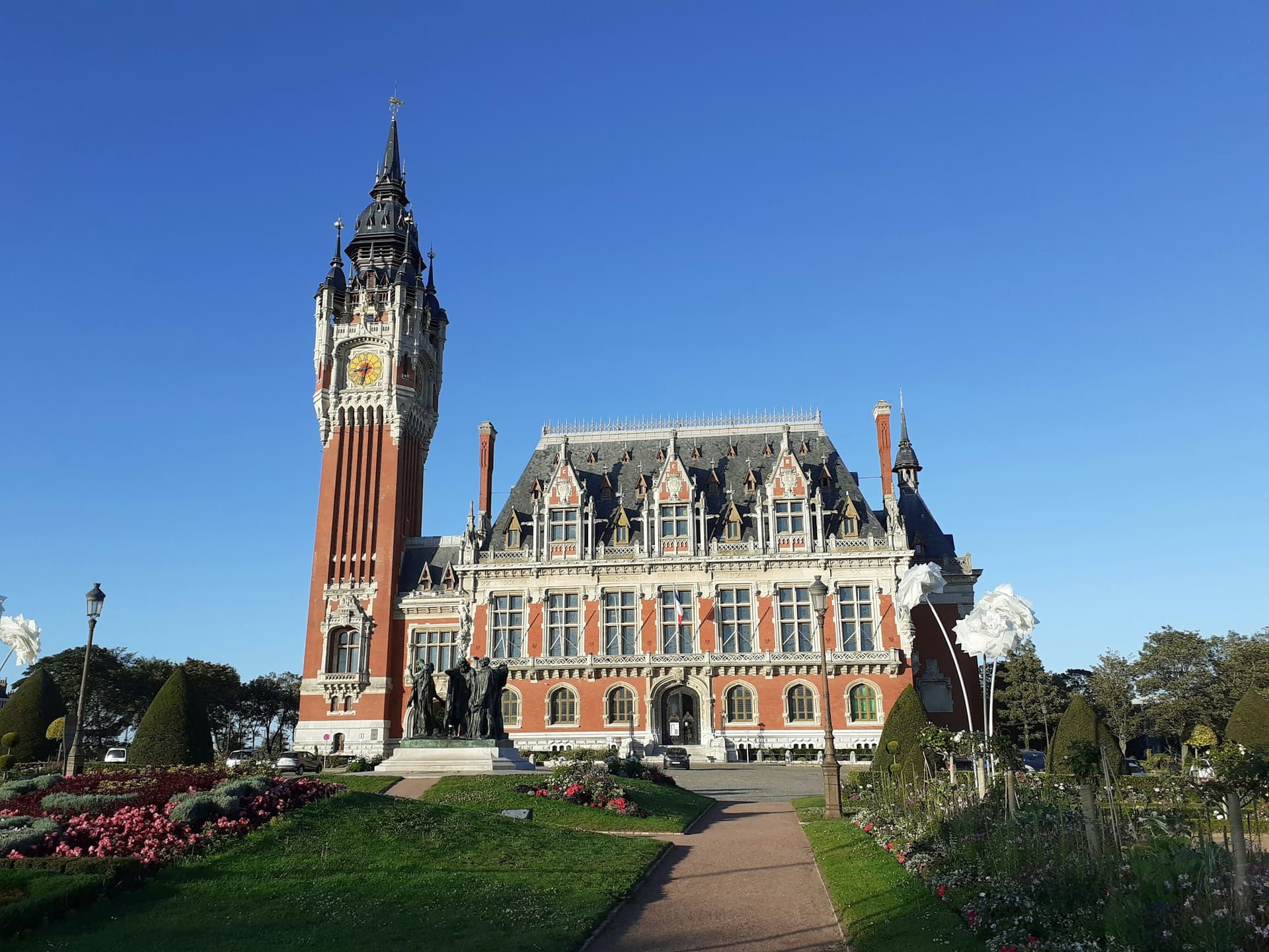Das Rathaus von Calais, Frankreich, im Morgenlicht, mit einem perfekt gepflegten Rasen im Vordergrund.