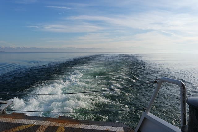 Scia lasciata da un traghetto in navigazione su un mare calmo sotto un cielo limpido.
