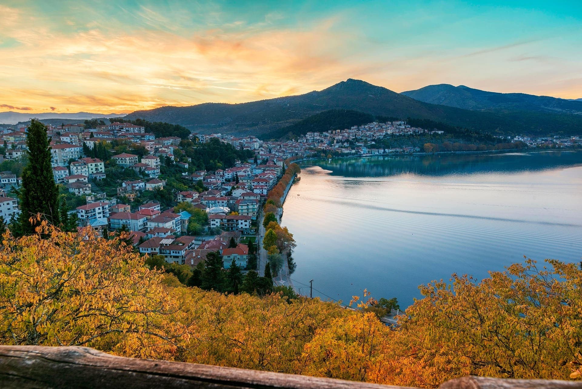 Une ville près d'un lac avec une montagne en fond et des arbres orangés en avant-plan.
