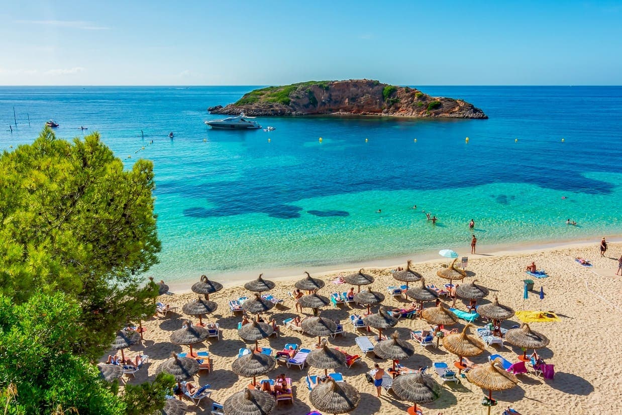 Pješčana plaža Portals Nous sa redovima suncobrana i pogledom na obližnji otočić na španjoskom otoku Mallorci.